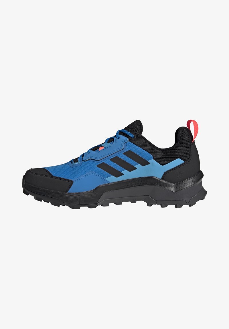 Chaussure de sport bleue et noire avec une tige texturée, une semelle en caoutchouc et trois bandes noires. Présente un accent rouge sur le talon et un système de laçage robuste.