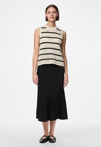 Κλασικό αμάνικο τοπ πλεκτό με κρεμ και μαύρες ρίγες, σε συνδυασμό με μακριά μαύρη φούστα. Τα παπούτσια είναι μαύρα φλατ, και το ύφασμα φαίνεται λείο και απαλό.