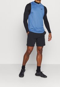 Blue sleeveless athletic shirt with black long sleeves, paired with black shorts and black shoes. Features Nike logo on the shirt.