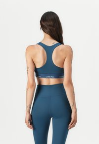 Blå sports-bh med racerback-design og en hvid "Calvin Klein" logo-bånd. Glat, strækbart stof i kombination med matchende højtaljede leggings.