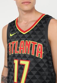 Man in zwarte Atlanta basketbaldataset met rode en gele accenten, nummer 17, en het Nike-logo op de borst.