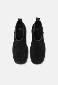 Crne suede slip-on cipele s zakrivljenim dizajnom, kontrastnim šavovima i malim potpeticama; mekana unutarnja obloga za udobnost.