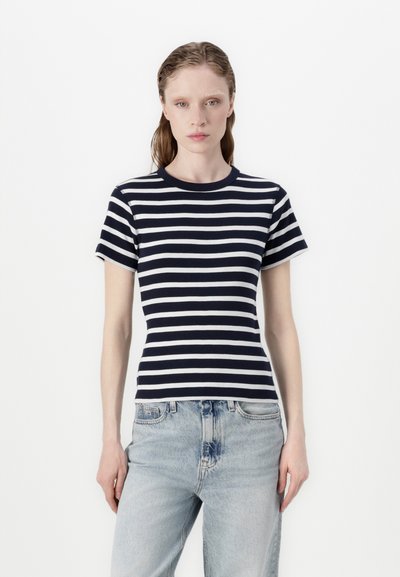 T-shirt à rayures bleu marine et blanches à manches courtes avec une texture côtelée et un col rond, associé à un jean délavé à coupe décontractée.