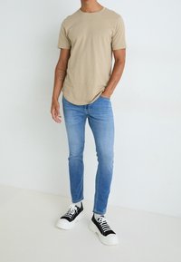 Béžové tričko s krátkým rukávem spárované s světle modrými slim fit džíny a černo-bílými teniskami. Tričko má kulatý výstřih.