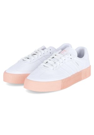 Białe sneakersy Adidas Samba z jasnoróżowymi, grubymi, teksturowanymi podeszwami i białymi sznurowadłami, widziane pod kątem na jednolitym białym tle.