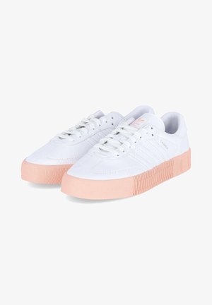 Zapatillas Adidas Samba blancas con suelas gruesas y texturizadas en rosa claro y cordones blancos, vistas en ángulo sobre un fondo blanco liso.