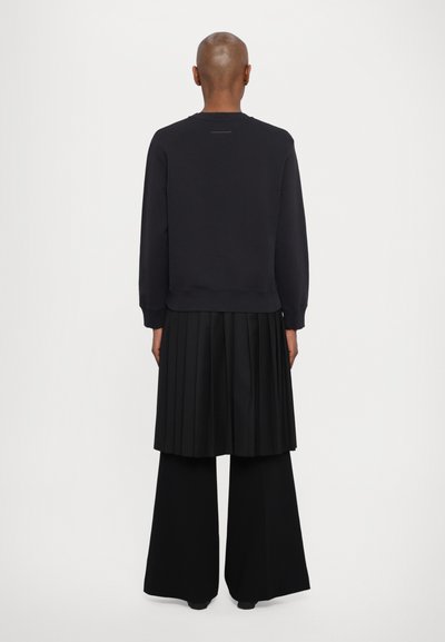 Μαύρο φούτερ με ριμπ μανίκια και τελείωμα, συνδυασμένο με πλισέ μαύρη φούστα και φαρδιά μαύρα παντελόνια, αεροφωτογραφία από πίσω.