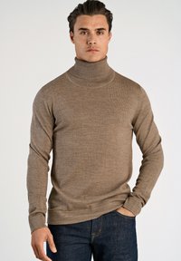 Brun polotröja med långa ärmar, tillverkad av stickat tyg. Har en figurnära passform och ribbad hals, bärs med mörka jeans.