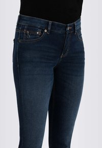 Tummansiniset farkut, joissa on kapea malli. Niissä on klassinen viiden taskun muotoilu ja kontrastiväriset tikkaus taskuissa ja saumoissa.