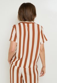 Top a maniche corte con righe verticali in ruggine e crema. Realizzato in tessuto morbido, presenta una vestibilità rilassata e piccole aperture laterali.