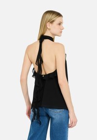 Top nero senza maniche con un profondo design sulla schiena, caratterizzato da dettagli a volant e un laccetto al collo. Abbinato a jeans in denim blu chiaro.