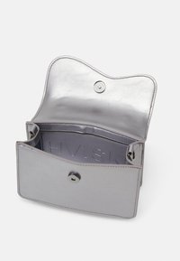 Bolso de mano plateado metálico con solapa redondeada, cierre a presión y marca embellecida en el interior. Textura suave y diseño minimalista.