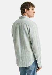 Camicia a maniche lunghe a righe in cotone verde chiaro e bianco. Presenta un colletto con bottone, una texture sottile e una piega sul retro.