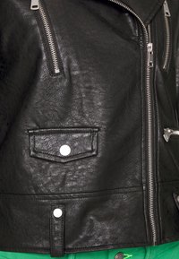 Svart lädermotorcykeljacka med silverfärgade dragkedjor, en klaffficka och tryckknappar, med en texturerad finish och figurpassad design.