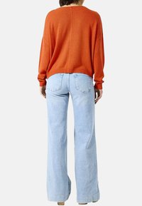 Overmaat oranje gebreide trui met geribbelde manchetten, gecombineerd met lichtblauwe flared jeans. Het ontwerp heeft een achternaad en een relaxed fit.