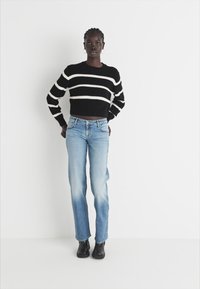 Black and white striped cropped sweater paired with light blue straight-leg jeans. Model wearing black ankle boots, minimalistic background.