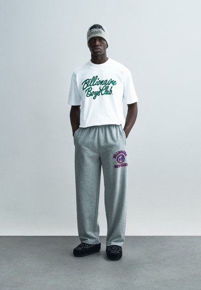 Λευκό κοντομάνικο μπλουζάκι με πράσινο κείμενο "Billionaire Boys Club", γκρι φόρμα με μοβ γράφημα και μαύρα παπούτσια χωρίς κορδόνια.