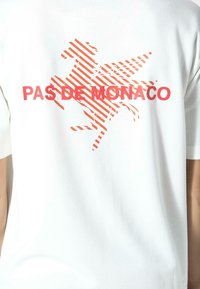 Camiseta blanca con un gráfico rojo de un caballo al galope y el texto "PAS DE MONACO" en la parte trasera. Material de algodón suave. Ajuste estándar.
