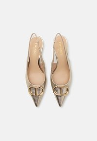 Metalické zlaté slingback ihličkové podpätky s špicatými prstami. Vyznačujú sa lesklým povrchom a veľkými zlatými prackami na prednej časti topánky. Mäkčené vnútorné podšívky.