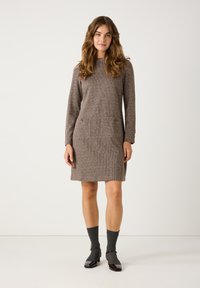 Brown checkered dress with long sleeves, two front pockets, and a high neckline. Paired with gray socks and burgundy patent leather shoes.
