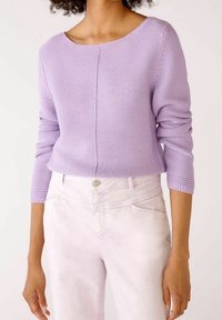 Lilac knit sweater with a rounded neckline and three-quarter sleeves, paired with light pink denim pants. Texture appears soft, and cozy.