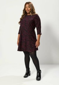 Burgunderfarbenes Kleid mit Muster, dreiviertelärmlig, abgerundetem Saum und floralem Design. Kombiniert mit schwarzen Stiefeletten und Strumpfhosen.