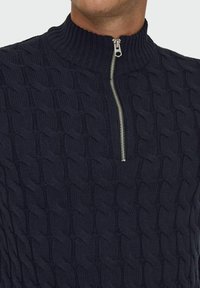 Navy Zip-Up-Pullover mit einem strukturierten Kabelstrickdesign und hohem Kragen. Akzent mit silbernem Metallreißverschluss. Weicher Strickstoff.