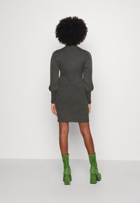 Šedé žebrované šaty s přiléhavým střihem, vysokým límcem a nabíranými dlouhými rukávy, doplněné zelenými semišovými kotníkovými botami.