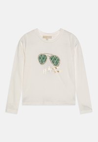 Camisa larga de manga larga color crema con un gráfico de gafas de sol verdes con patrón, contorneadas por tachuelas doradas, y "Michael Kors" escrito en dorado debajo.