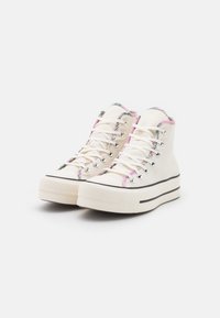 Hochhackige.Canvas-Sneaker in Off-White mit lebhaftem floralem Besatz, rosa Akzenten, Metallösen und schwarzen Gummisohlen. Strukturiertes Muster auf der Sohle.