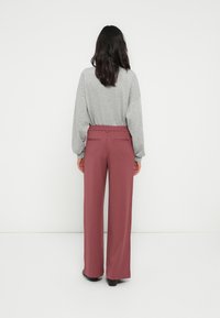 Gray long-sleeve top paired with high-waisted, wide-leg pants in muted burgundy. The outfit features smooth fabric and subtle back pocket details.