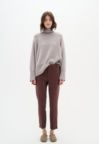 Gaiši pelēks pārmērīgi liels turtlenecks džemperis, kombinēts ar pieguļošām bordo biksēm ar sānu izgriezumiem un mīkstām brūnām slip-on kurpēm.