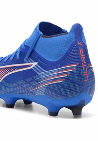 Crampon de football bleu avec une tige en maille texturée et des accents rouges. Il présente un design épuré et un talon sculpté avec des crampons moulés pour une traction optimale.