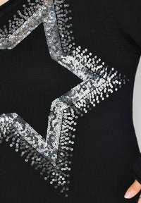 Maglione nero lavorato a maglia con una grande stella argentata di paillettes, decorata con un intricato motivo di paillettes lucide lungo i bordi.