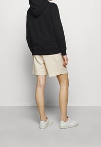 Sudadera negra con capucha, pantalones cortos beiges y zapatillas blancas. Tejido suave, corte relajado y diseño minimalista. Sin patrones ni acentos visibles.