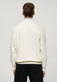 Kremasta majica s kapuco, sprovedena v udobnem kroju, z ribastimi manšeti in robom ter zaobljenim izrezom. V kombinaciji s temnimi hlačami. Gladka tekstura.