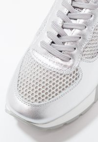 Basket argentée avec dessus en tissu mesh, empiècements en cuir métallisé, lacets gris et semelle en caoutchouc blanche.