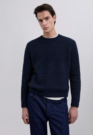 Suéter de cuello redondo azul marino hecho de una suave tela texturizada, combinado con jeans de un azul oscuro. Presenta un ajuste relajado y puños acanalados.