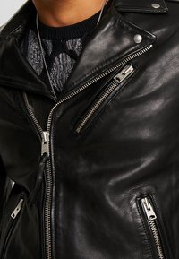 Svart läder bikerjacka med silverfärgade dragkedjor, med en klassisk krage, flera fickor med dragkedja och en mjuk yta.