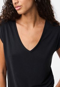 Juoda V formos kaklo marškinėliai su trumpomis rankovėmis, minkštu audiniu ir laisvu kirpimu, išryškinantys lygią medžiagą be raštų ar puošmenų.