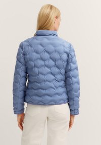 Steppjacke in Hellblau, mit einem gesteppten Design, hohem Kragen und taillierten Ärmeln. Glatte Textur mit einem cropped Schnitt auf der Taille.