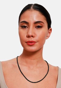 Collana nera intrecciata con una superficie liscia, indossata attorno al collo, in contrasto con una maglietta chiara. Nessun ulteriore abbellimento.