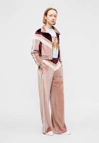 Σετ βελούδινη φόρμα σε απαλό ροζ χρώμα με διαγώνιες ρίγες σε κρεμ και βουργουνδί. Περιλαμβάνει cropped σακάκι και παντελόνι με φαρδιά μπατζάκια. Γραφικό μπλουζάκι με αρκούδα.