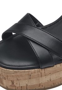 Black platform sandals with crossed leather straps and a textured cork sole. The sole has visible natural patterns for added detail.