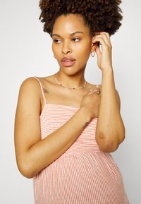 Vestido listrado, sem mangas, em tecido suave rosa e branco, com um corpete ajustado e uma saia solta. Joias simples e um tatuagem discreta visíveis.