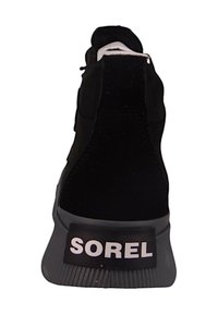 Schwarzer Sneaker von hinten betrachtet, mit einer dicken Gummisohle und dem "SOREL"-Logo in weiß auf einem schwarzen Patch über der Sohle.
