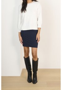 Suéter blanco y acogedor con mangas tres cuartos; falda azul marino ajustada; botas negras de cuero hasta la rodilla con punta afilada.