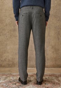 Gray wool trousers with a textured finish, featuring patch pockets and two buttons on the back, paired with dark shoes.