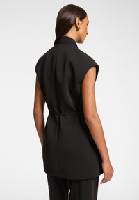 Blazer senza maniche nero con vita cinturata, colletto alto, spalle strutturate e tessuto liscio; la vista posteriore mostra linee pulite e una vestibilità tailored.