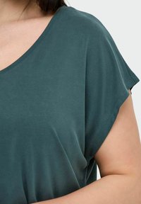 Teal short-sleeve shirt with a rounded neckline. Soft, smooth fabric with a relaxed fit, showing partial arm and shoulder.